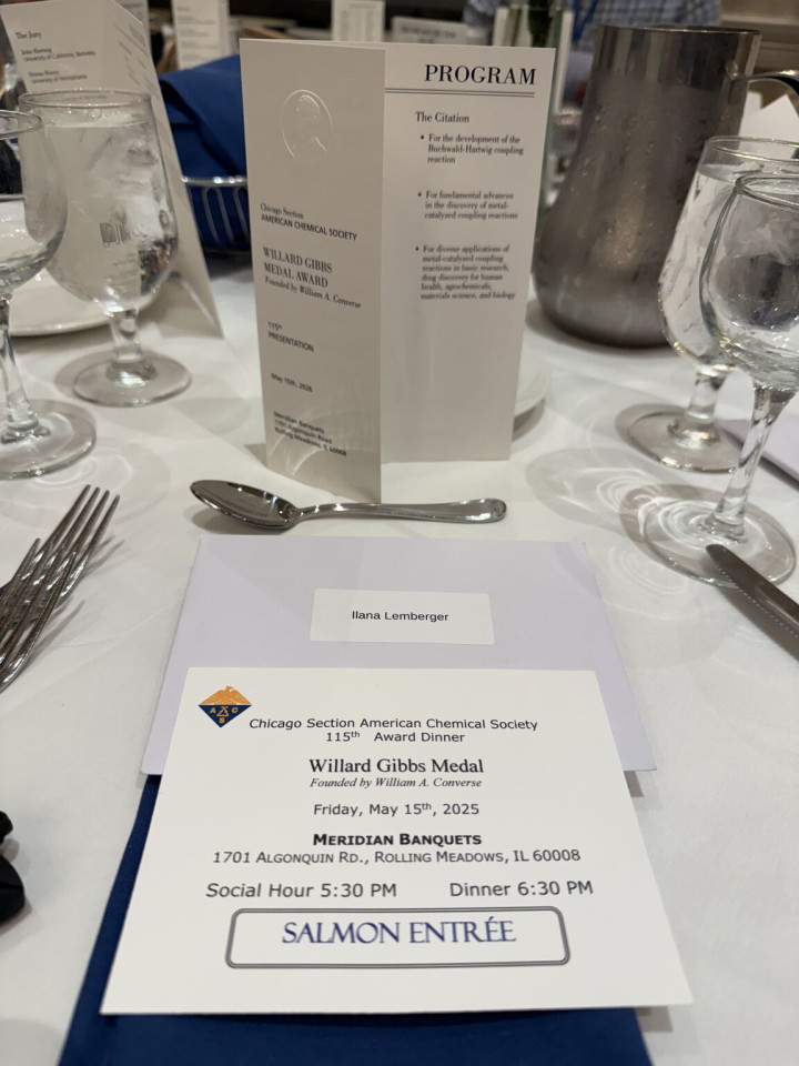 Photo of one of the banquet place settings, with neatly-arranged formal dishes and silverware, plus a program card with the embossed image of the Gibbs Medal, and a meal card designating a 