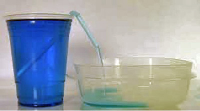 Photo of a tall cup filled with blue liquid on the left, and low container on the right, and a straw dipped into the tall cup so that some blue liquid can be pulled up into the straw and flow into the low container