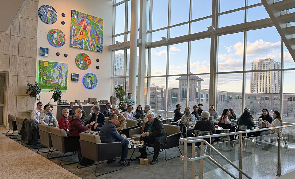 Photo of a couple dozen chemists enjoying boxed sandwich dinners in Loyola's sunny third floor Quinlan Hall lounge
