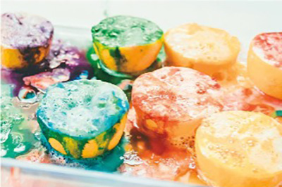 Photo of a dish with several lemons cut in half, face-up, with food coloring and powder covering their acidic faces 