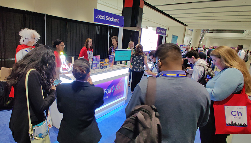 Photo of the Chicago Section welcome booth at ACS Fall 2026, staffed with volunteers and a mannequin of Alice Hamilton, and half-suffounded by many meeting attendees playing a Jeopardy-like chemistry game